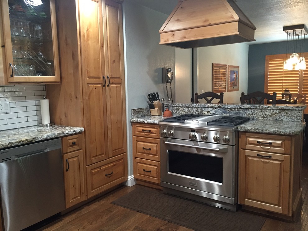 Mid-sized mountain style u-shaped medium tone wood floor kitchen photo with an undermount sink, raised-panel cabinets, light wood cabinets, granite countertops, white backsplash, ceramic backsplash and stainless steel appliances