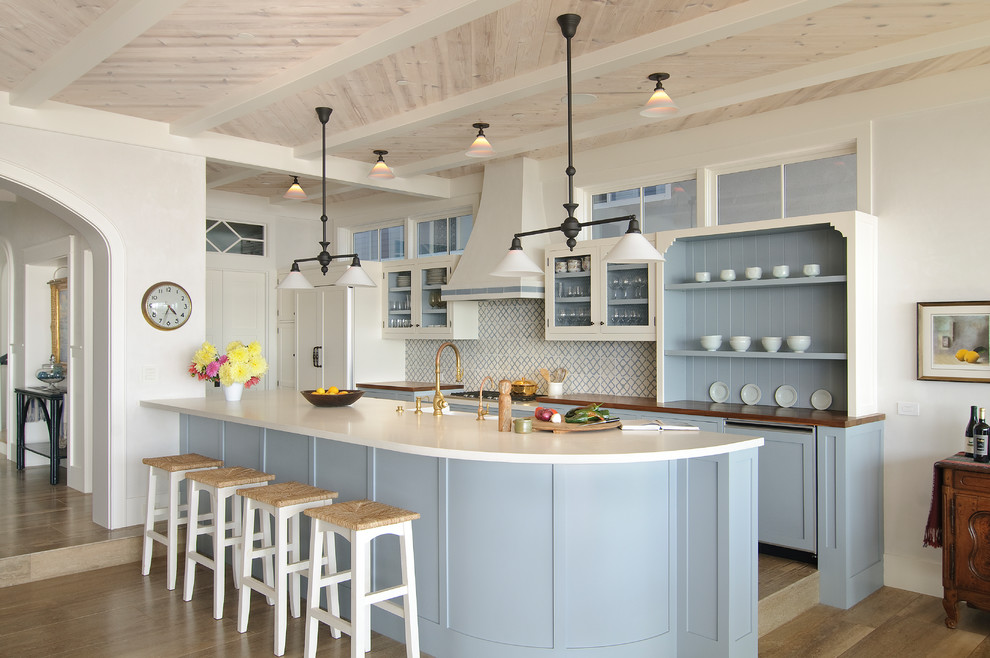 Inspiration for a beach style galley kitchen in Los Angeles with a farmhouse sink, shaker cabinets, blue cabinets, white splashback, panelled appliances, a peninsula, brown floor, white benchtop, quartz benchtops, cement tile splashback and limestone floors.