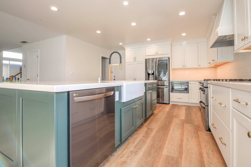 Photo of a large country l-shaped eat-in kitchen in Sacramento with a farmhouse sink, shaker cabinets, green cabinets, quartz benchtops, white splashback, stone tile splashback, stainless steel appliances, vinyl floors, with island, brown floor and white benchtop.