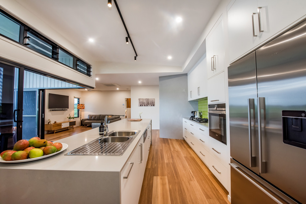 Large contemporary galley open plan kitchen in Other with a double-bowl sink, flat-panel cabinets, white cabinets, granite benchtops, green splashback, ceramic splashback, stainless steel appliances, vinyl floors, with island, white benchtop and vaulted.