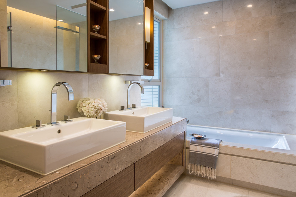 This is an example of a contemporary bathroom in Hong Kong with a vessel sink, an alcove tub, beige tile and beige benchtops.