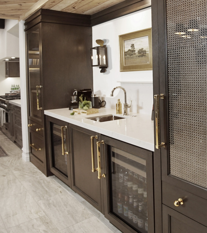 Design ideas for a mid-sized transitional single-wall wet bar in Phoenix with an undermount sink, glass-front cabinets, dark wood cabinets, quartz benchtops, grey splashback, engineered quartz splashback, travertine floors, grey floor and grey benchtop.