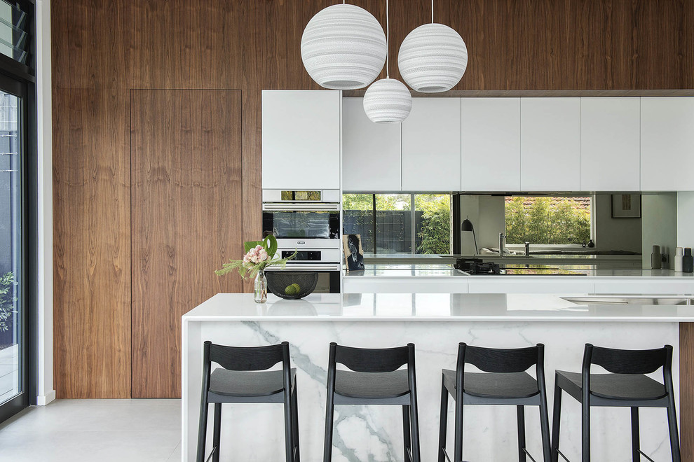 This is an example of a contemporary galley kitchen in Perth with an undermount sink, flat-panel cabinets, medium wood cabinets, mirror splashback, stainless steel appliances, with island, white floor and white benchtop.