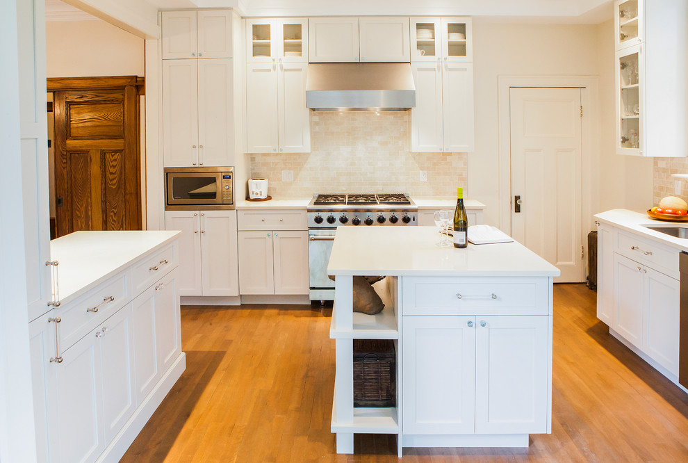 This is an example of a mid-sized transitional u-shaped separate kitchen in Montreal with an undermount sink, shaker cabinets, white cabinets, quartz benchtops, beige splashback, stone tile splashback, stainless steel appliances, light hardwood floors and with island.