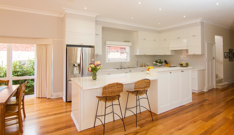 Inspiration for a mid-sized traditional l-shaped open plan kitchen in Melbourne with a double-bowl sink, shaker cabinets, white cabinets, granite benchtops, white splashback, porcelain splashback, stainless steel appliances, medium hardwood floors and with island.