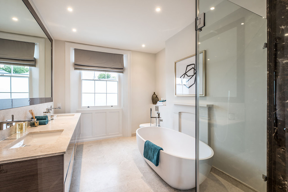 Photo of a contemporary master bathroom in London with white walls, an undermount sink, flat-panel cabinets, a freestanding tub, beige tile and stone tile.