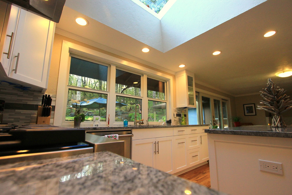 Large transitional u-shaped light wood floor open concept kitchen photo with an undermount sink, shaker cabinets, white cabinets, granite countertops, multicolored backsplash, mosaic tile backsplash, stainless steel appliances and an island