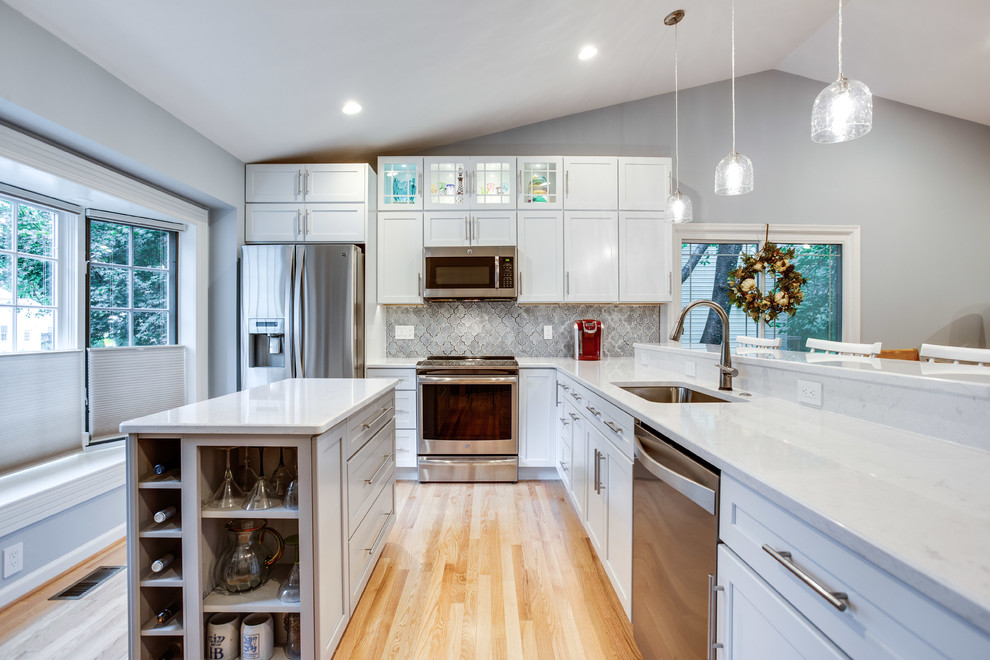 Photo of a large transitional u-shaped kitchen in DC Metro with an undermount sink, shaker cabinets, quartz benchtops, stainless steel appliances, medium hardwood floors, with island and white benchtop.