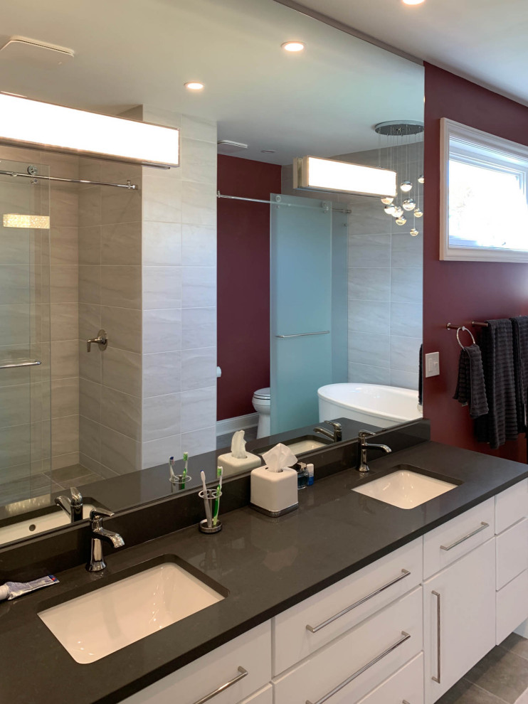Large contemporary master bathroom in Cleveland with flat-panel cabinets, white cabinets, a freestanding tub, an alcove shower, a one-piece toilet, gray tile, porcelain tile, red walls, porcelain floors, an undermount sink, quartzite benchtops, grey floor, a sliding shower screen, black benchtops, an enclosed toilet, a double vanity and a built-in vanity.