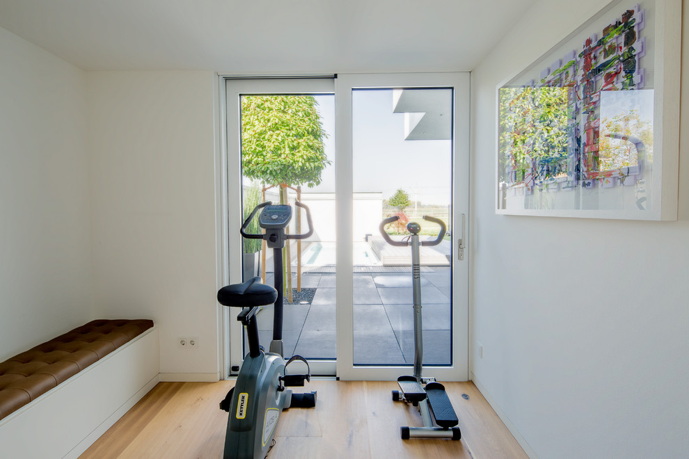 This is an example of a small contemporary multipurpose gym in Dusseldorf with white walls, medium hardwood floors and beige floor.