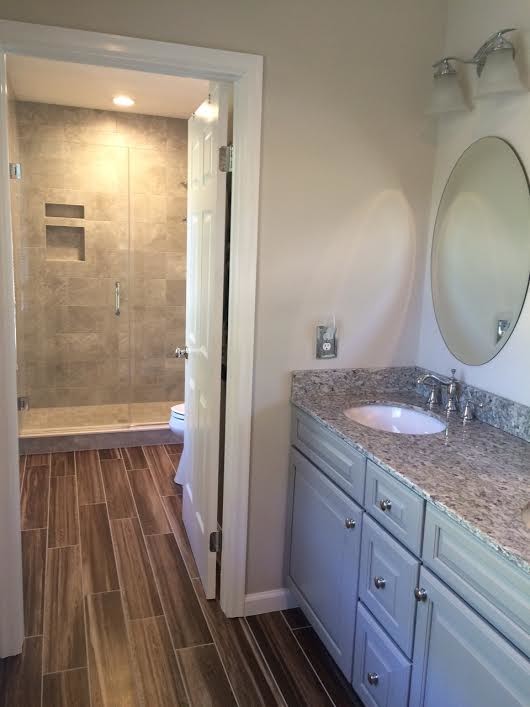 This is an example of a traditional bathroom in Baltimore with an undermount sink, raised-panel cabinets, grey cabinets, granite benchtops, an alcove shower, a two-piece toilet, gray tile, porcelain tile, grey walls and porcelain floors.