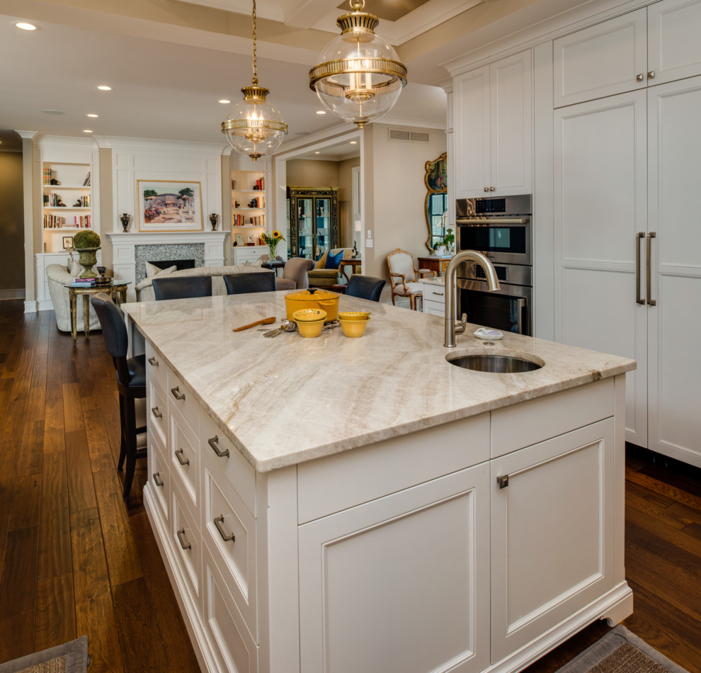 Large transitional u-shaped eat-in kitchen in Detroit with an undermount sink, beaded inset cabinets, white cabinets, quartzite benchtops, white splashback, subway tile splashback, panelled appliances, medium hardwood floors, with island, brown floor and beige benchtop.