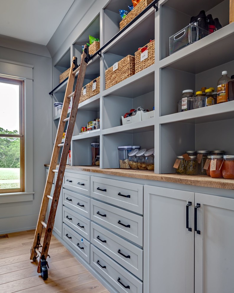 This is an example of a large country single-wall kitchen pantry in Nashville with wood benchtops, a farmhouse sink, shaker cabinets, white cabinets, white splashback, subway tile splashback, stainless steel appliances, medium hardwood floors, with island, brown floor and white benchtop.