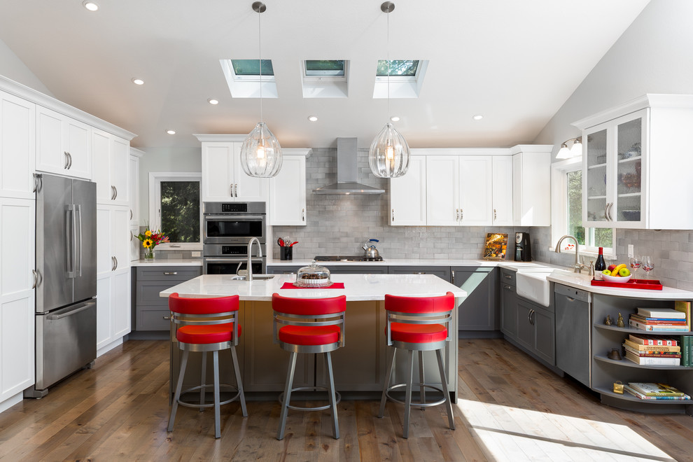 This is an example of a large transitional u-shaped eat-in kitchen in San Francisco with a farmhouse sink, raised-panel cabinets, grey cabinets, quartz benchtops, grey splashback, porcelain splashback, stainless steel appliances, medium hardwood floors and with island.