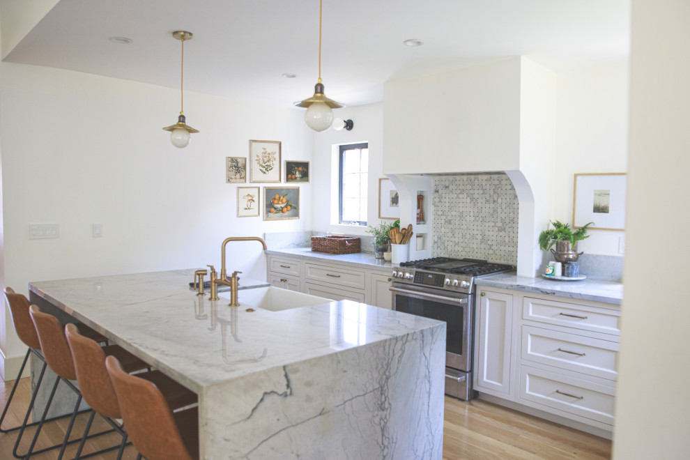 Mid-sized transitional l-shaped light wood floor and brown floor open concept kitchen photo with a farmhouse sink, shaker cabinets, beige cabinets, quartzite countertops, gray backsplash, stone slab backsplash, paneled appliances, an island and gray countertops