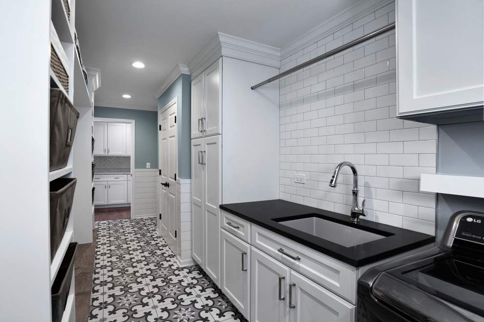 This is an example of a mid-sized transitional galley dedicated laundry room in Chicago with an undermount sink, recessed-panel cabinets, white cabinets, granite benchtops, blue walls, ceramic floors, a side-by-side washer and dryer, multi-coloured floor and black benchtop.
