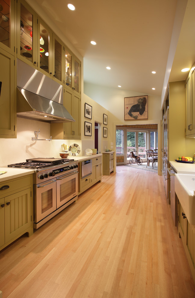 Photo of a large transitional galley separate kitchen in San Francisco with a farmhouse sink, beaded inset cabinets, green cabinets, quartz benchtops, white splashback, stone slab splashback, stainless steel appliances and light hardwood floors.