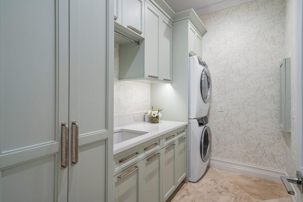 Large transitional single-wall utility room in Miami with an undermount sink, recessed-panel cabinets, blue cabinets, beige walls, a stacked washer and dryer, beige floor, white benchtop and wallpaper.