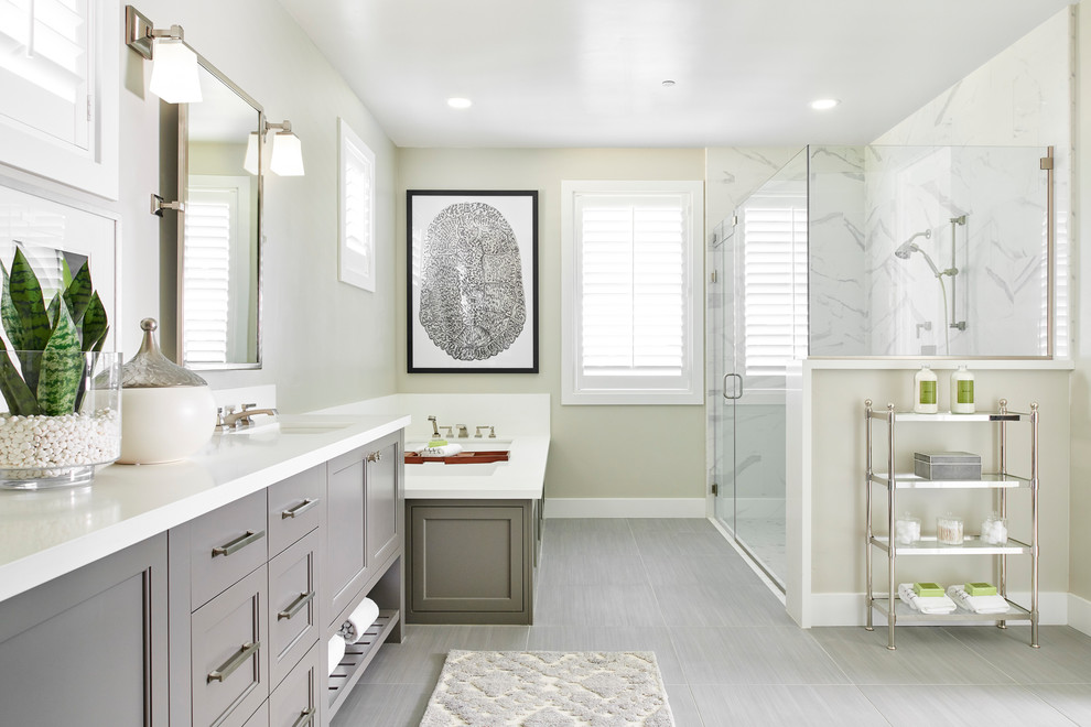 Photo of a transitional bathroom in San Francisco with recessed-panel cabinets, grey cabinets, an undermount tub, a corner shower, white tile, beige walls, an undermount sink, grey floor, a hinged shower door and white benchtops.