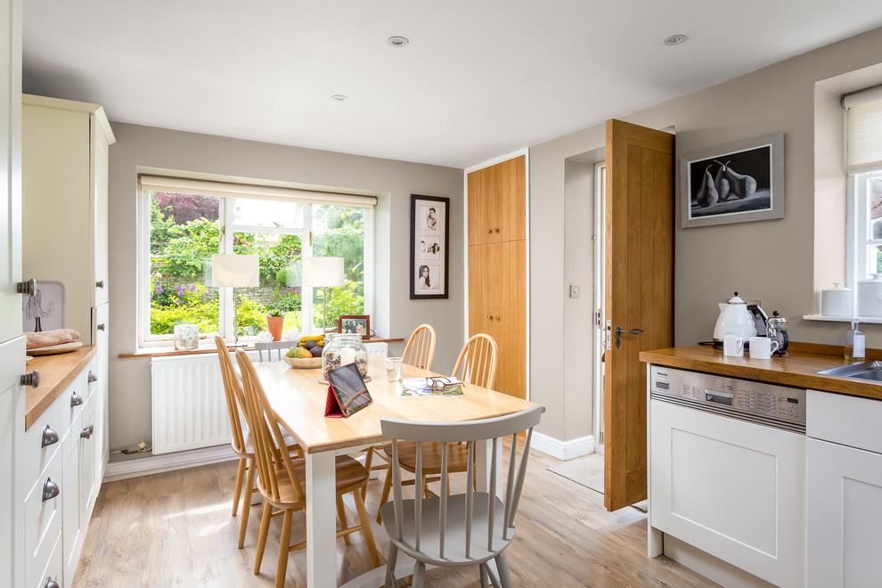 This is an example of a mid-sized country u-shaped eat-in kitchen in Gloucestershire with a drop-in sink, shaker cabinets, wood benchtops, stainless steel appliances, no island, white cabinets, light hardwood floors and beige floor.