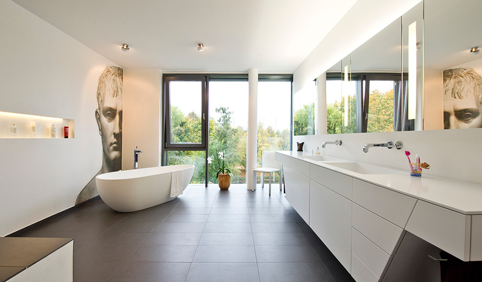 Photo of a contemporary master bathroom in Berlin with flat-panel cabinets, white cabinets, a freestanding tub, white walls, an integrated sink and gray tile.