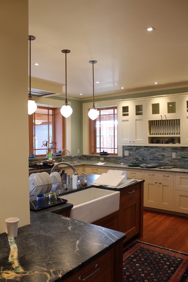 Photo of a large arts and crafts u-shaped separate kitchen in Other with a farmhouse sink, glass-front cabinets, white cabinets, granite benchtops, grey splashback, stone tile splashback, stainless steel appliances, medium hardwood floors, with island, brown floor and green benchtop.