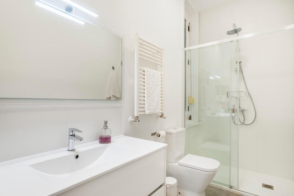 Modelo de cuarto de baño moderno grande con armarios tipo mueble, puertas de armario blancas, ducha abierta, sanitario de pared, suelo de baldosas de porcelana, aseo y ducha y suelo gris