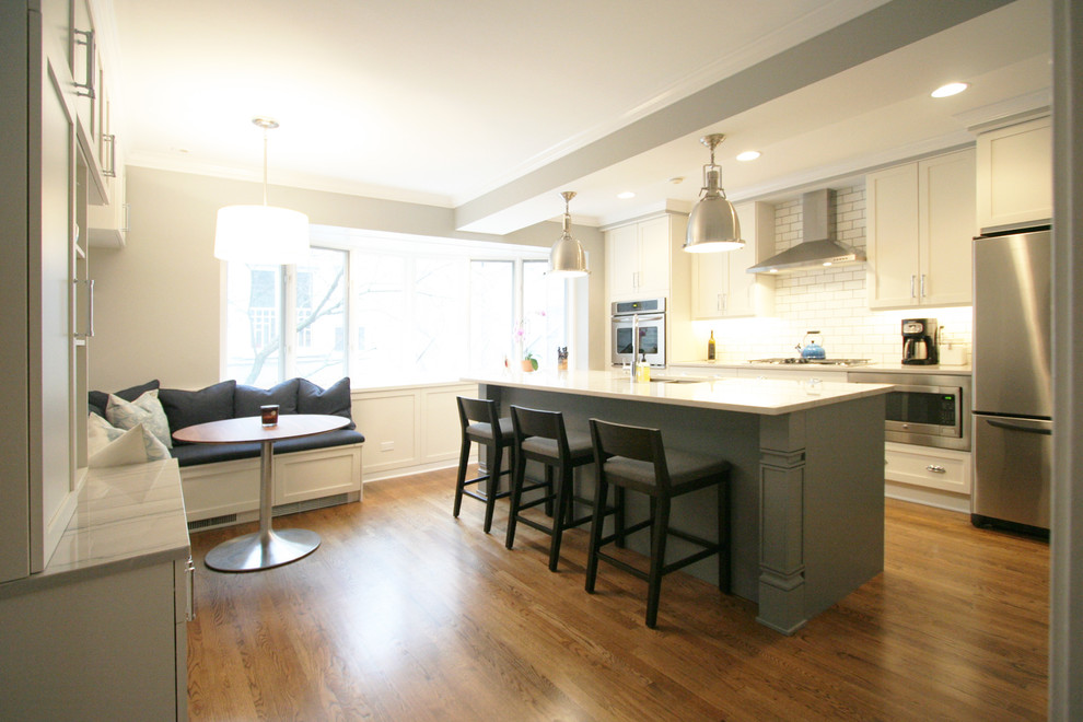 Large transitional medium tone wood floor kitchen photo in Chicago with an undermount sink, shaker cabinets, white cabinets, quartzite countertops, white backsplash, subway tile backsplash, stainless steel appliances and an island