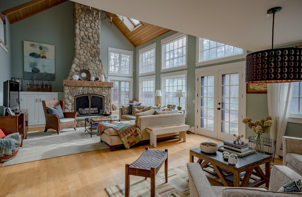 Photo of a large country formal open concept living room in Boston with green walls, light hardwood floors, a wood stove, a stone fireplace surround, brown floor and no tv.