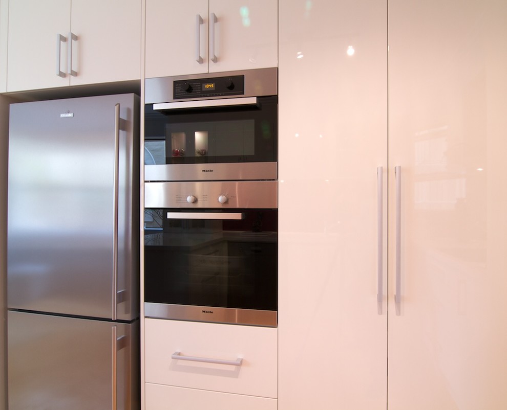 Design ideas for a small modern u-shaped separate kitchen in Sydney with an integrated sink, flat-panel cabinets, white cabinets, solid surface benchtops, red splashback, glass sheet splashback, stainless steel appliances, light hardwood floors and no island.