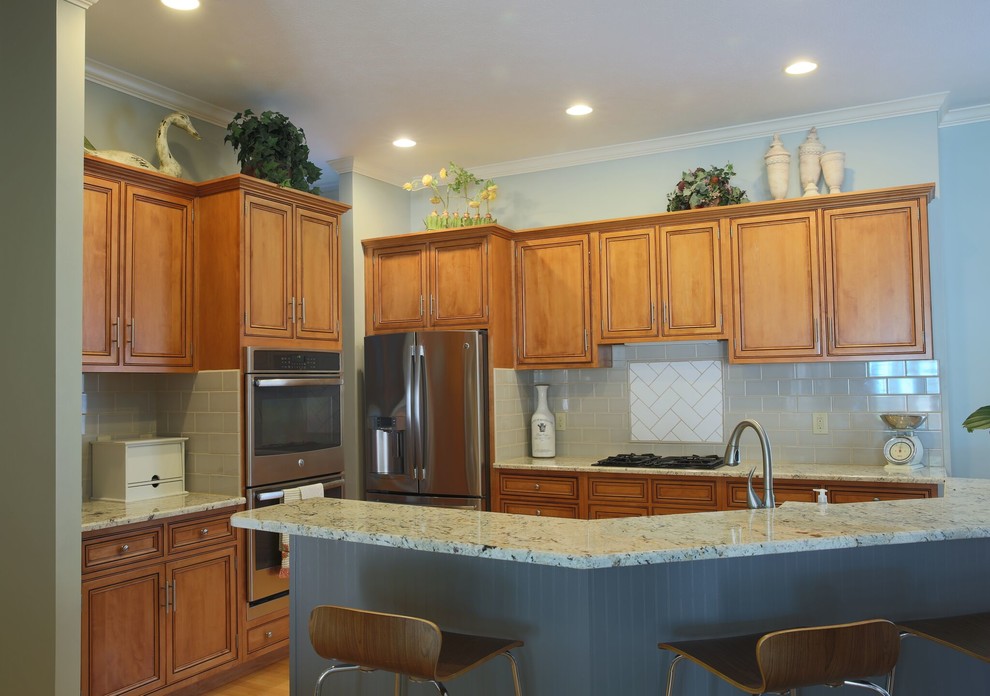 Small transitional u-shaped medium tone wood floor and brown floor eat-in kitchen photo in Indianapolis with a drop-in sink, shaker cabinets, medium tone wood cabinets, quartz countertops, blue backsplash, subway tile backsplash, stainless steel appliances and a peninsula