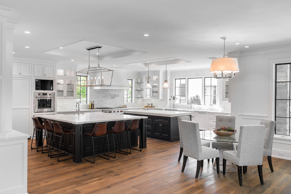 Transitional eat-in kitchen in Los Angeles with shaker cabinets, white cabinets, white splashback, stainless steel appliances, medium hardwood floors and multiple islands.
