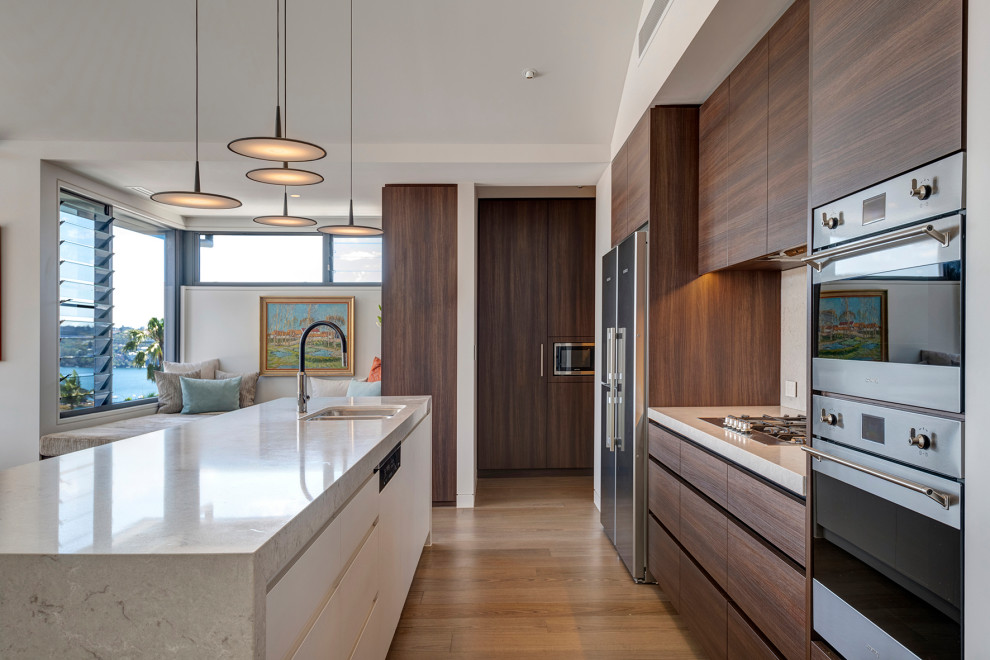 Design ideas for a large contemporary open plan kitchen in Sydney with dark wood cabinets, engineered stone countertops, stainless steel appliances, an island and brown floors.