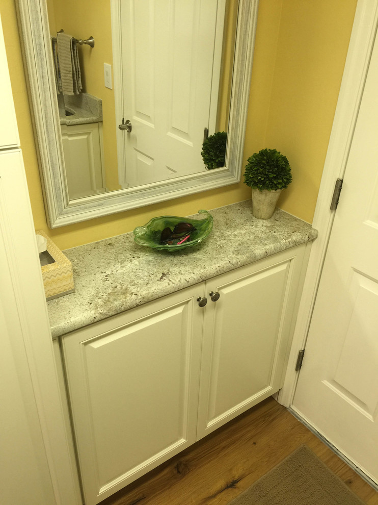Photo of a small transitional galley dedicated laundry room in Miami with an undermount sink, raised-panel cabinets, white cabinets, granite benchtops, yellow walls, medium hardwood floors and a side-by-side washer and dryer.