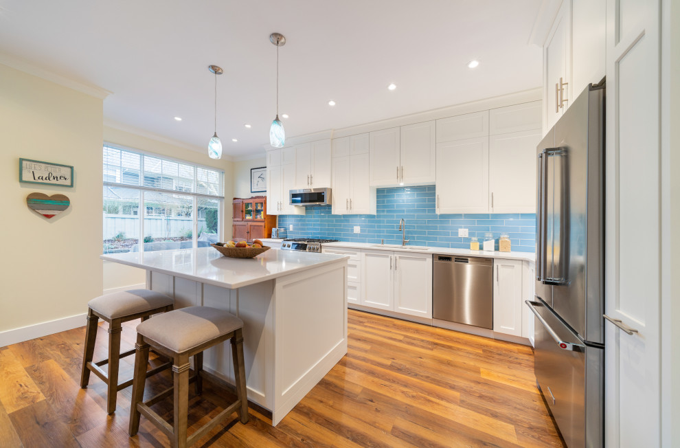 Eat-in kitchen - large coastal l-shaped medium tone wood floor and brown floor eat-in kitchen idea in Vancouver with an undermount sink, shaker cabinets, white cabinets, quartz countertops, blue backsplash, subway tile backsplash, stainless steel appliances, an island and white countertops