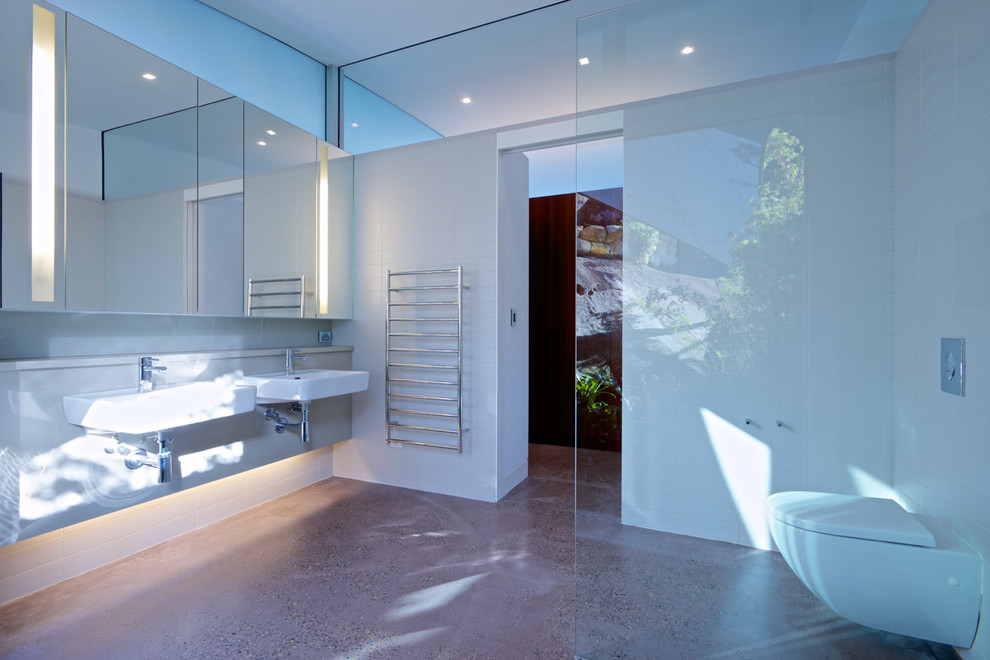 Inspiration for a mid-sized contemporary master bathroom in Sydney with glass-front cabinets, white cabinets, an open shower, a wall-mount toilet, white tile, ceramic tile, white walls, concrete floors, a wall-mount sink, engineered quartz benchtops, grey floor, an open shower and white benchtops.