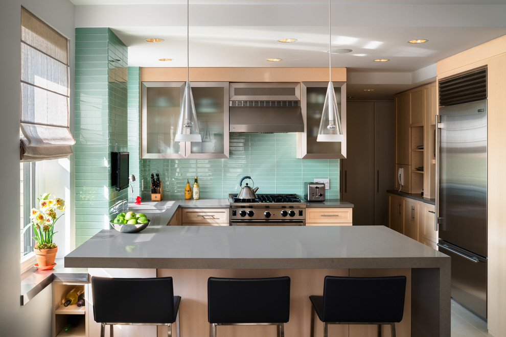 This is an example of a contemporary u-shaped eat-in kitchen in New York with glass-front cabinets, light wood cabinets, glass tile splashback and stainless steel appliances.