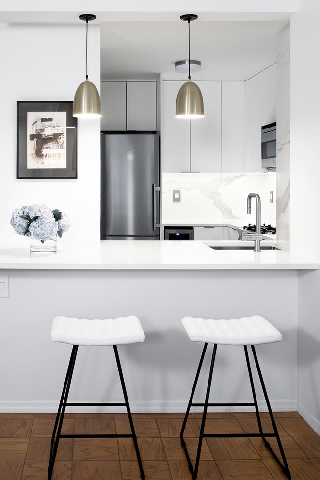 Inspiration for a small modern u-shaped eat-in kitchen in New York with flat-panel cabinets, white cabinets, quartz benchtops, white splashback, porcelain splashback, stainless steel appliances, an undermount sink, light hardwood floors, a peninsula and beige floor.