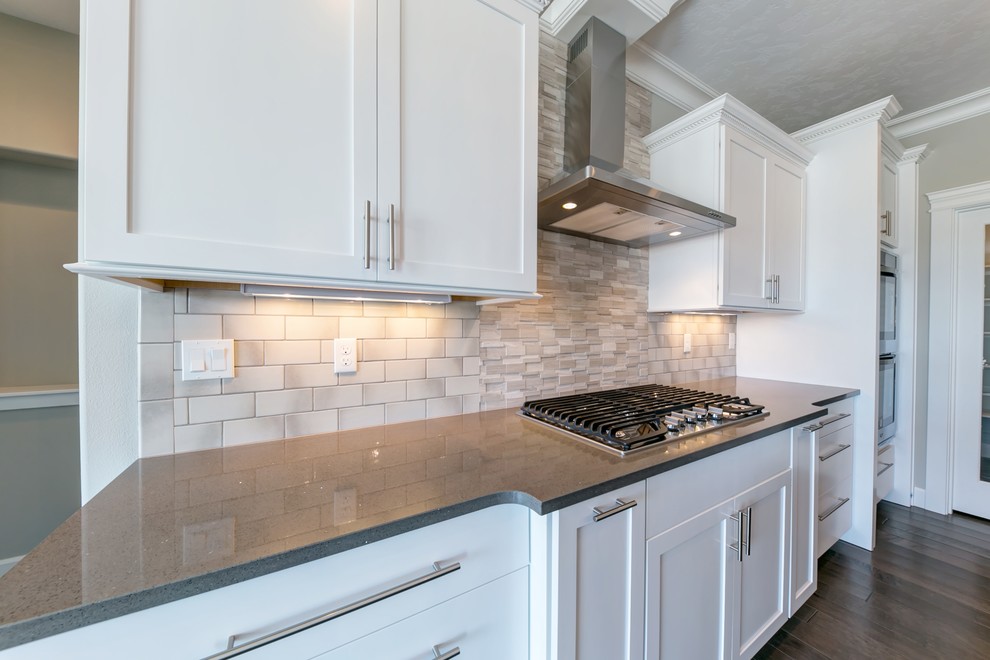 This is an example of a large transitional l-shaped open plan kitchen in Seattle with an undermount sink, shaker cabinets, white cabinets, quartz benchtops, white splashback, porcelain splashback, stainless steel appliances, medium hardwood floors and with island.