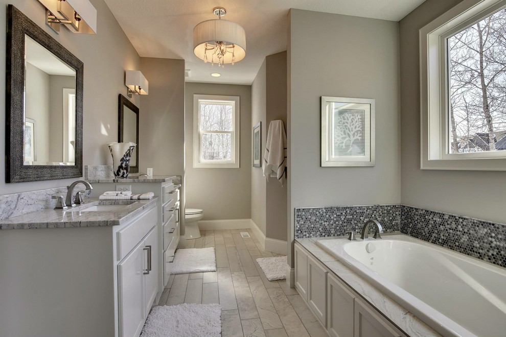 Photo of a large transitional master bathroom in Minneapolis with shaker cabinets, white cabinets, a drop-in tub, an alcove shower, a one-piece toilet, black tile, gray tile, white tile, mosaic tile, grey walls, porcelain floors, an undermount sink and granite benchtops.