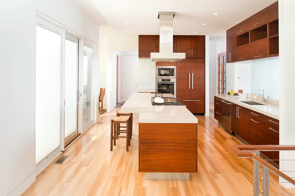 Inspiration for a mid-sized contemporary l-shaped open plan kitchen in Cleveland with an undermount sink, flat-panel cabinets, dark wood cabinets, stainless steel appliances, light hardwood floors, with island, solid surface benchtops and brown floor.