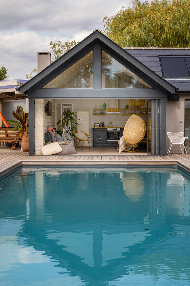 Design ideas for a mid-sized beach style courtyard rectangular pool in Sussex with a pool house and decking.