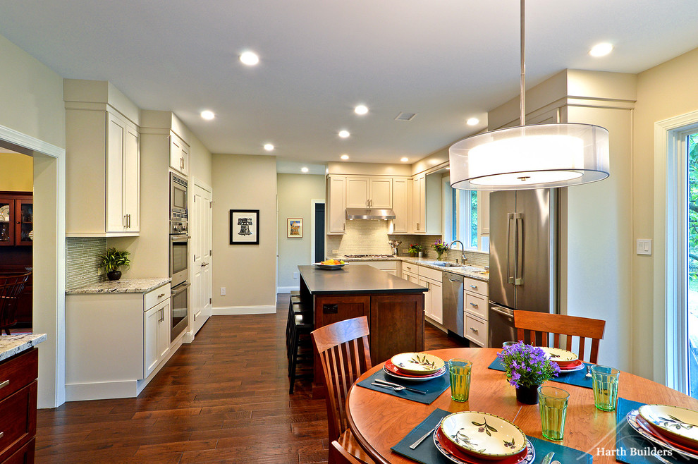 Inspiration for a mid-sized transitional l-shaped medium tone wood floor eat-in kitchen remodel in Philadelphia with an undermount sink, recessed-panel cabinets, white cabinets, granite countertops, gray backsplash, glass tile backsplash, stainless steel appliances and an island