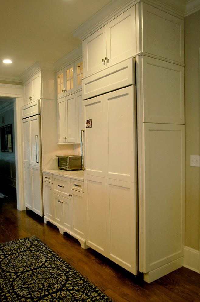 This is an example of a large traditional l-shaped eat-in kitchen in New York with an undermount sink, recessed-panel cabinets, white cabinets, marble benchtops, white splashback, panelled appliances, medium hardwood floors and with island.