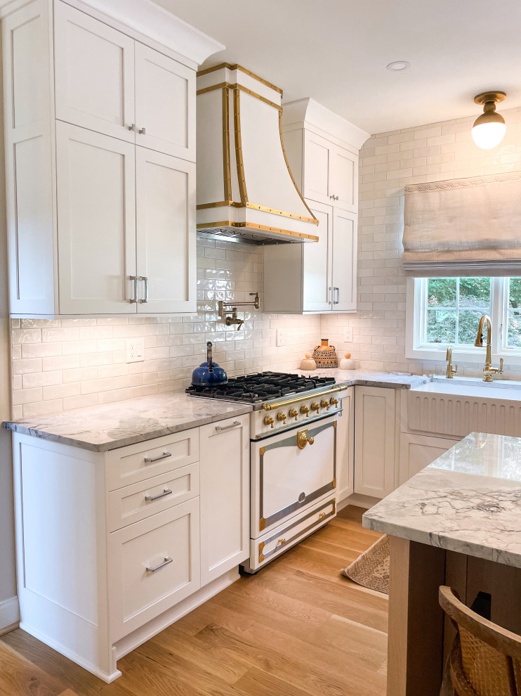 Foto på ett stort vintage vit kök, med en rustik diskho, skåp i shakerstil, vita skåp, bänkskiva i kvartsit, vitt stänkskydd, stänkskydd i tunnelbanekakel, rostfria vitvaror, mellanmörkt trägolv, en köksö och beiget golv