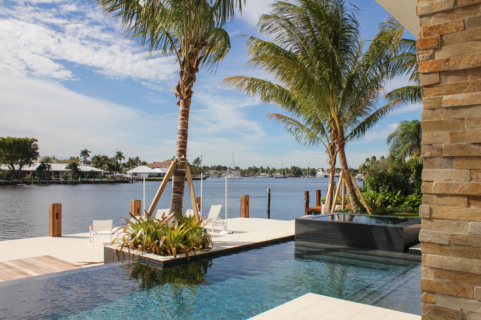 Large modern backyard custom-shaped infinity pool in Miami with a hot tub and decking.