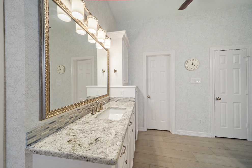 Photo of a medium sized contemporary ensuite bathroom in Houston with raised-panel cabinets, white cabinets, a freestanding bath, a corner shower, a two-piece toilet, white tiles, ceramic tiles, white walls, ceramic flooring, a submerged sink, granite worktops, white floors, a hinged door, grey worktops, a shower bench, double sinks, a built in vanity unit, a coffered ceiling and wallpapered walls.