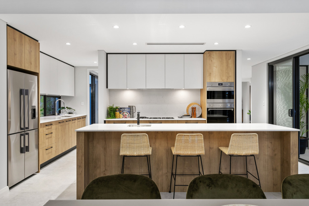 Contemporary l-shaped kitchen in Perth with an undermount sink, flat-panel cabinets, white cabinets, white splashback, stone slab splashback, stainless steel appliances, with island, grey floor and white benchtop.