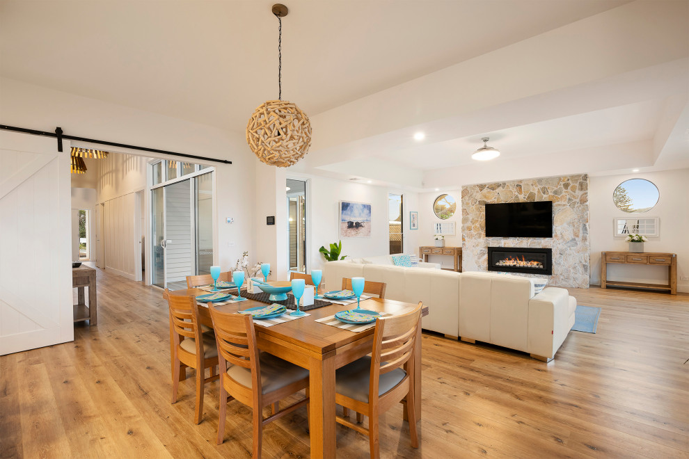 Design ideas for a large beach style open plan dining in Melbourne with white walls, laminate floors, a standard fireplace, a stone fireplace surround and brown floor.