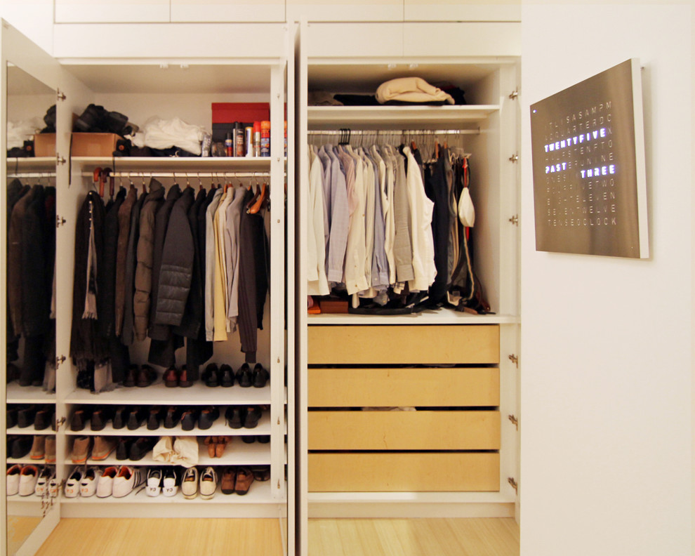 This is an example of a mid-sized modern men's built-in wardrobe in New York with open cabinets, white cabinets, bamboo floors and beige floor.